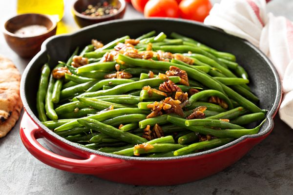 Sauteed green beans in a skillet with candied pecans