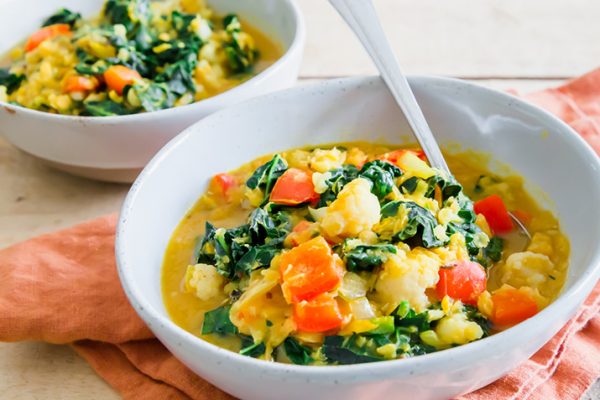 Two bowls of hearty, red lentil stew with kale on a table