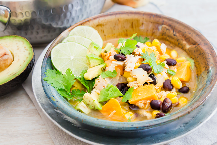 Bowl of Chipotle Lime Chicken and Veggie Soup with beans, sweet potatoes and lime wedges